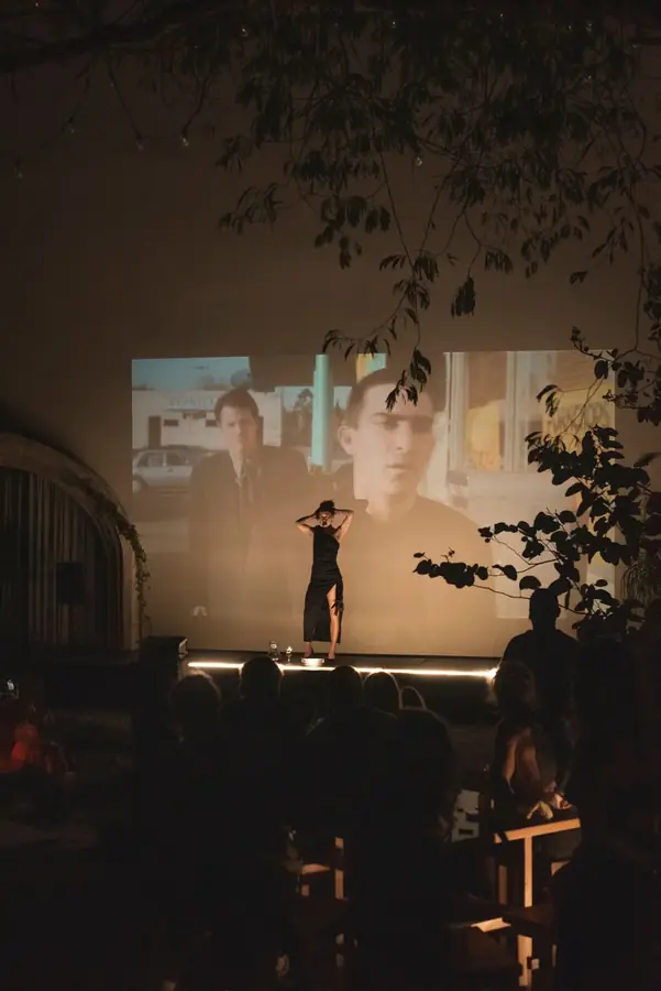 Público sentado al aire libre viendo un performance frente a una gran proyección de video en Tulum