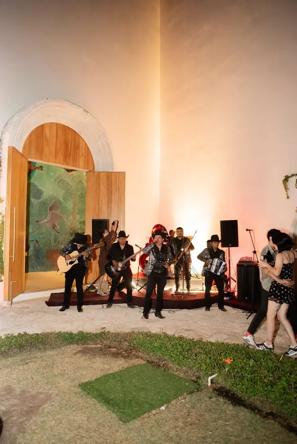 Banda norteña tocando en vivo junto a un portón de madera mientras una pareja baila